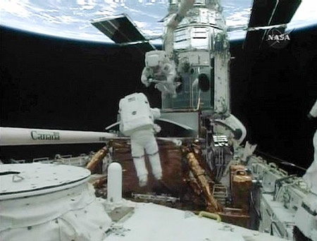 Spacewalker John Grunsfeld (L) prepares the old Wide Field Planetary Camera for storage in Atlantis's payload bay as Drew Feustel (top), attached to the robot arm, looks on in this image from NASA TV May 14, 2009.